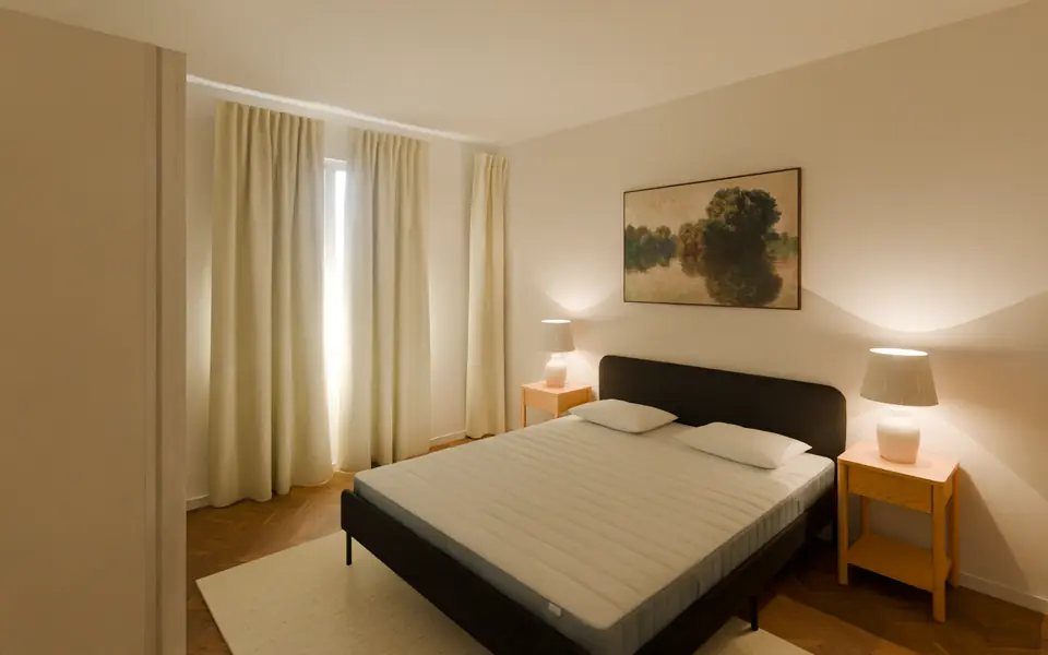 Schlafzimmer mit Doppelbett, Parkett und bodentiefen Vorhängen